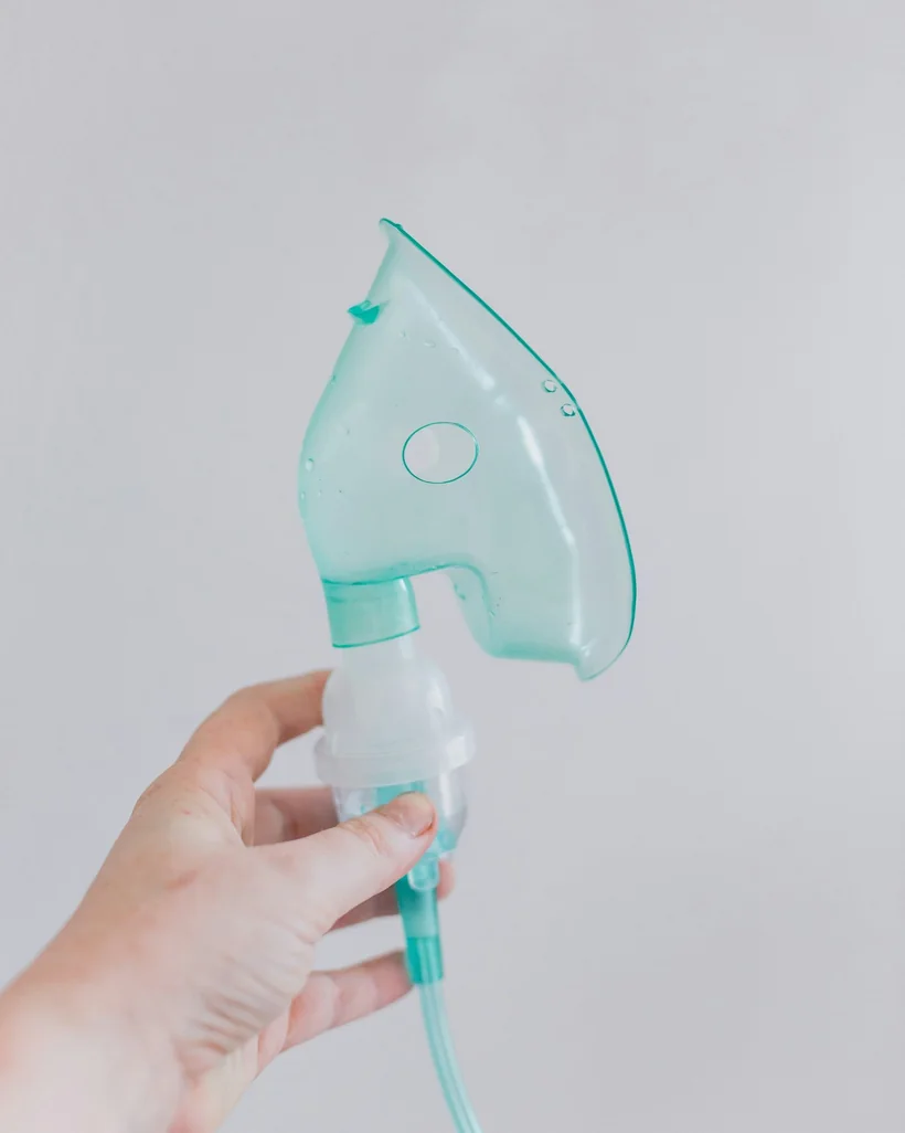 Mano sosteniendo una mascarilla de nebulización de color turquesa