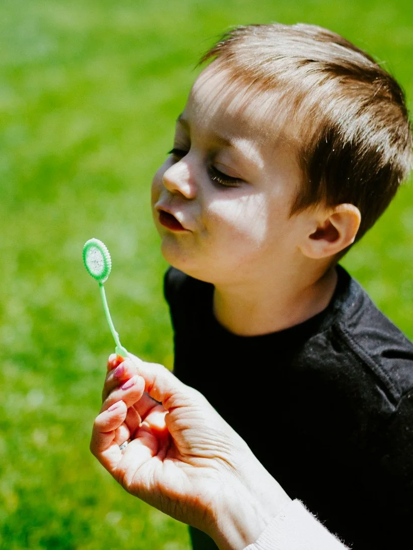 Niño soplando burbujas al aire libre, imagen simbólica de soplar con fuerza como en la espirometría